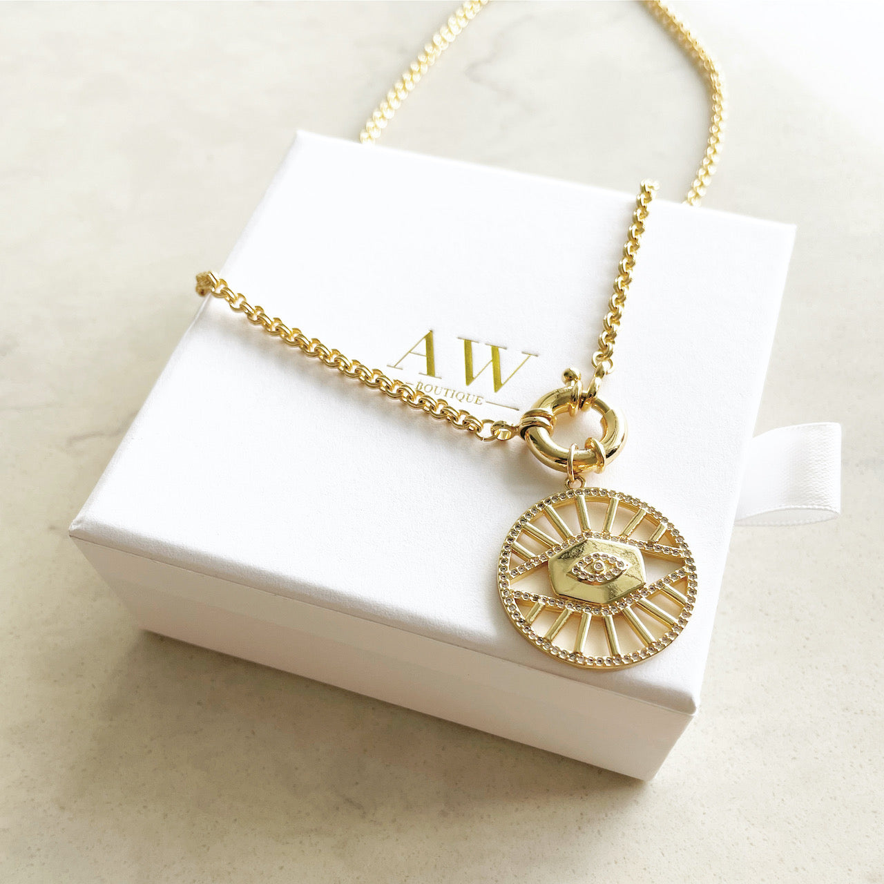 Gold filled evil eye medallion pendant charm necklace. This is a bold gold necklace design. Australian jewellery brand AW Boutique.  The necklace is sitting on top of an AW Boutique white gift box.