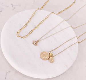 Flat lay photo of AW Boutique's Paperclip Chain Necklace, Mini Crystal Evil Eye Necklace, and the Dual Evil Eye Coin Necklace.  Gold filled jewellery by Australian jewellery brand AW Boutique.