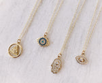 Load image into Gallery viewer, AW Boutique gold filled jewellery. All Seeing Eye or Eye of Providence pendant charm on a dainty fine 16 inch cable necklace chain. Part of the Protection collection.  Shown in this image as a flat lay next to the Mini Blue Evil Eye Necklace, the Small Crystal Hamsa Necklace, and the Mini Crystal Evil Eye Necklace.
