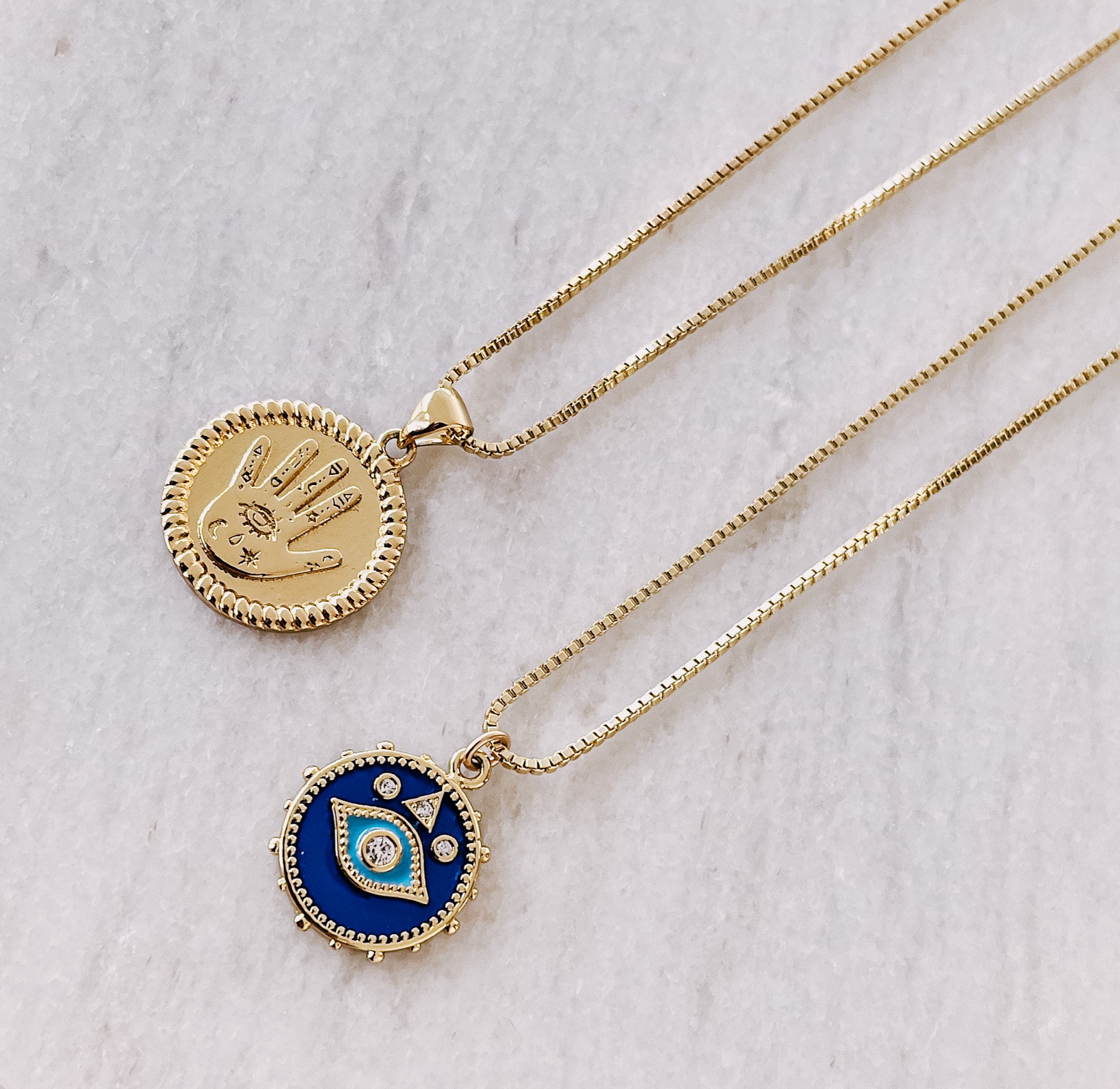 AW Boutique's gold filled jewellery. 18 inch box chain with vintage evil eye enamel coin shaped pendant necklace.  This image shows the Vintage Evil Eye Enamel Necklace in a flat lay image with the Vintage Hamsa Coin Necklace.